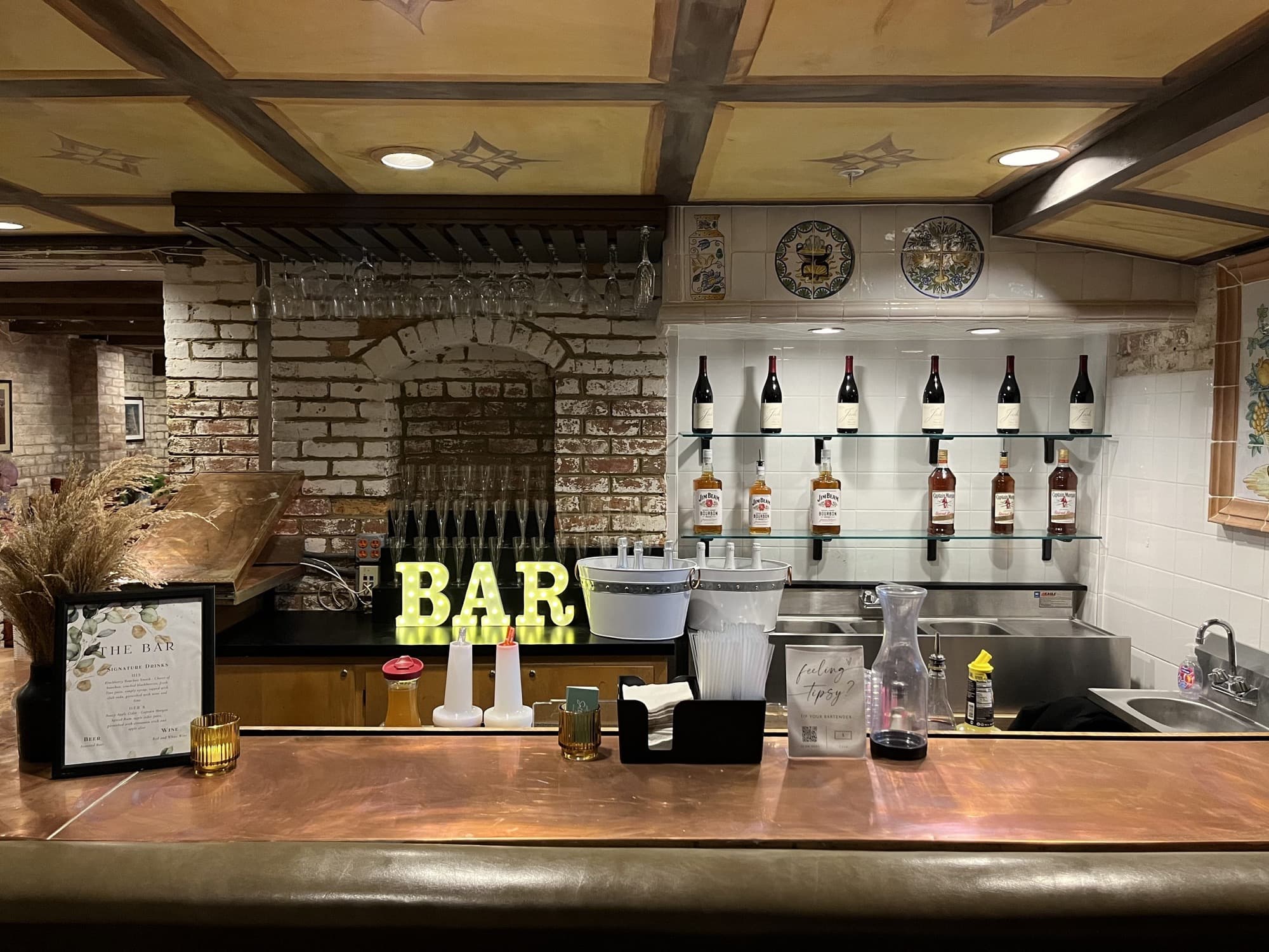 The Pop Up Bar with lit BAR letters beneath a shelf of bottles in a warm venue room with exposed brick.