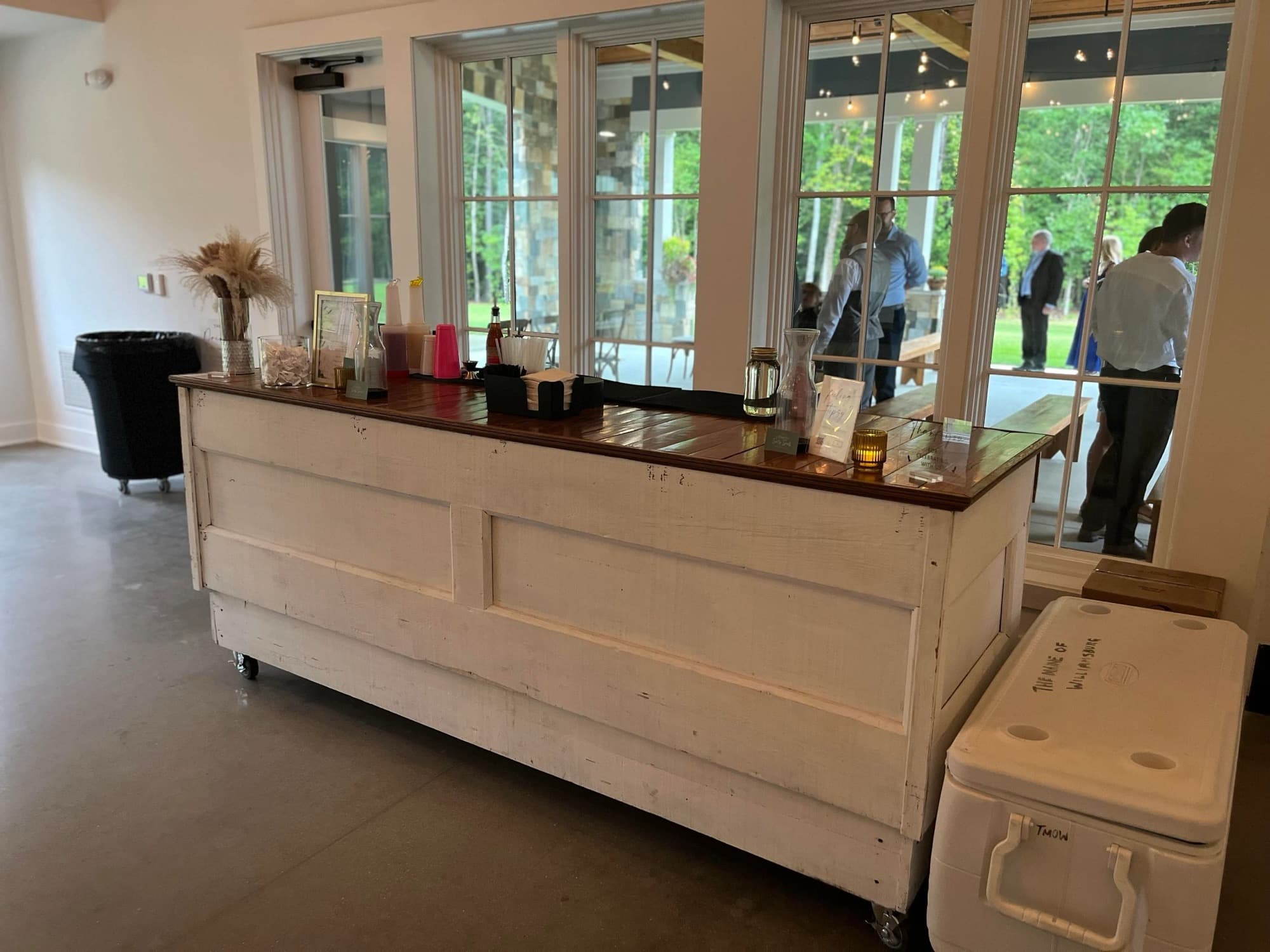 The Pop Up Bar set up in a bright venue with tall windows, a cooler beside it and guests in the room.